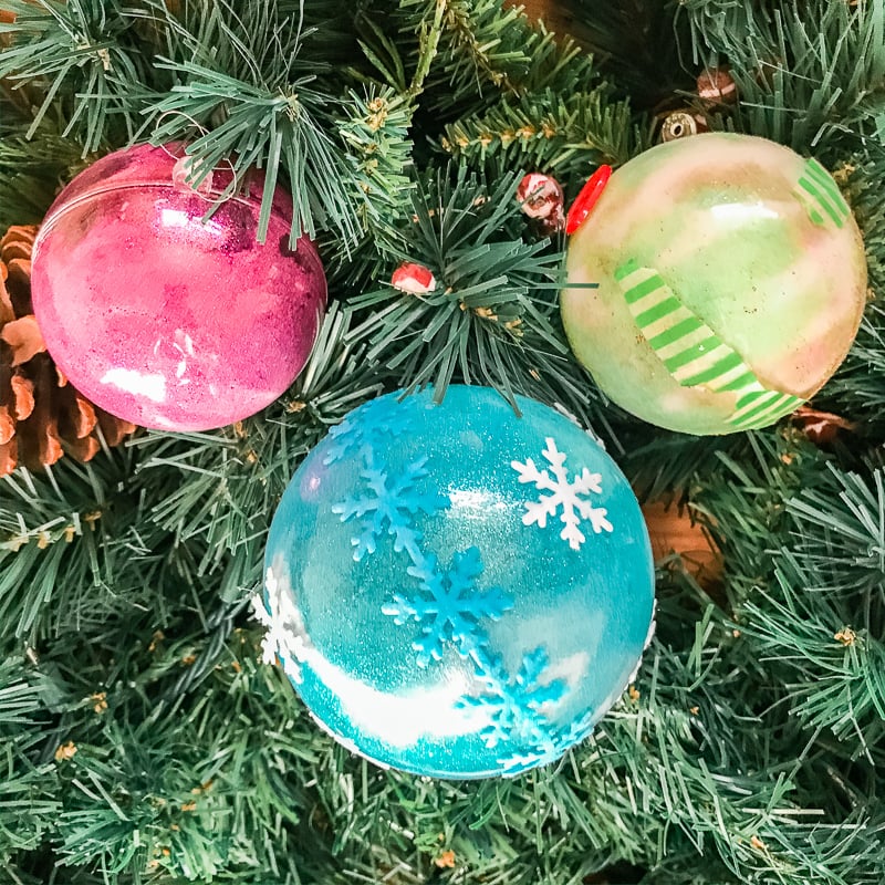 Three DIY glitter ornaments hanging on a tree.