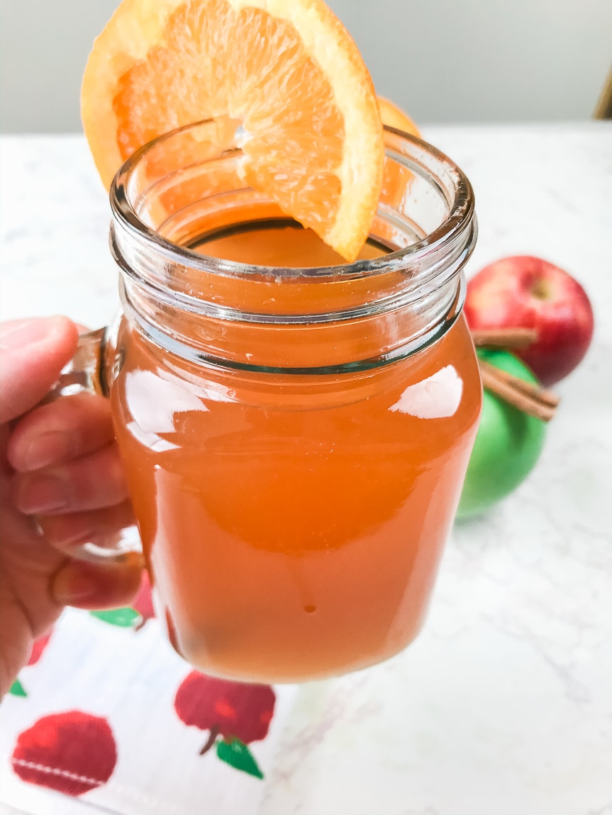A hand holding a glass of homemade instant pot apple cider.