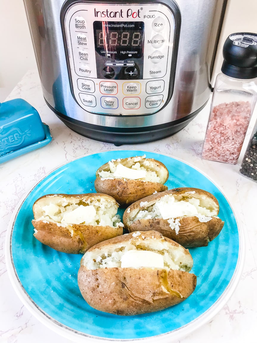 A plate of four baked potatoes in front of an instant pot.