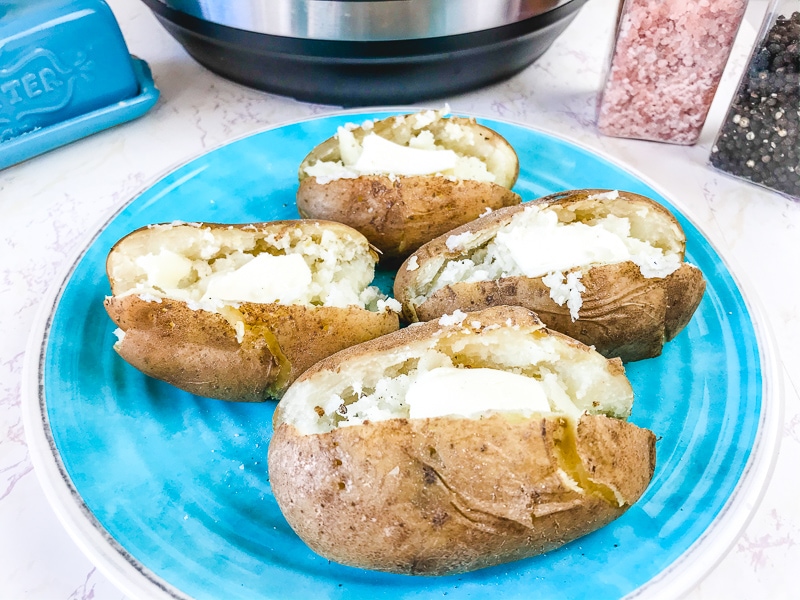 A blue plate with four baked potatoes on it.
