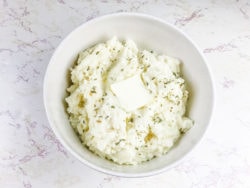 A bowl of Keto cauliflower mashed potatoes with a slice of butter on top.