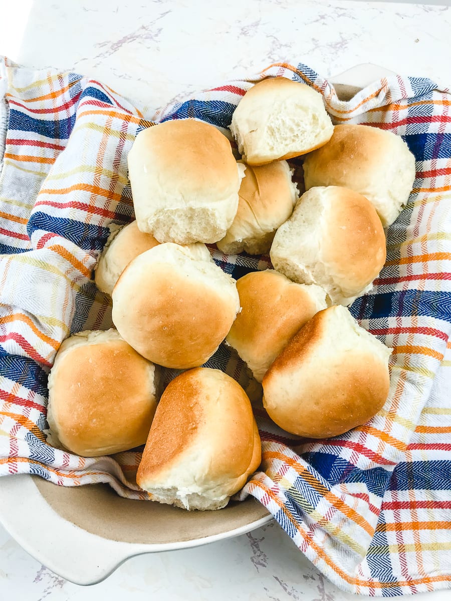 A basket of Parker house rolls lined with a blue and red striped towel.