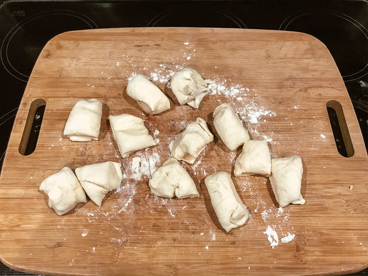 12 pieces of Parker house roll dough ready to be rolled into balls.