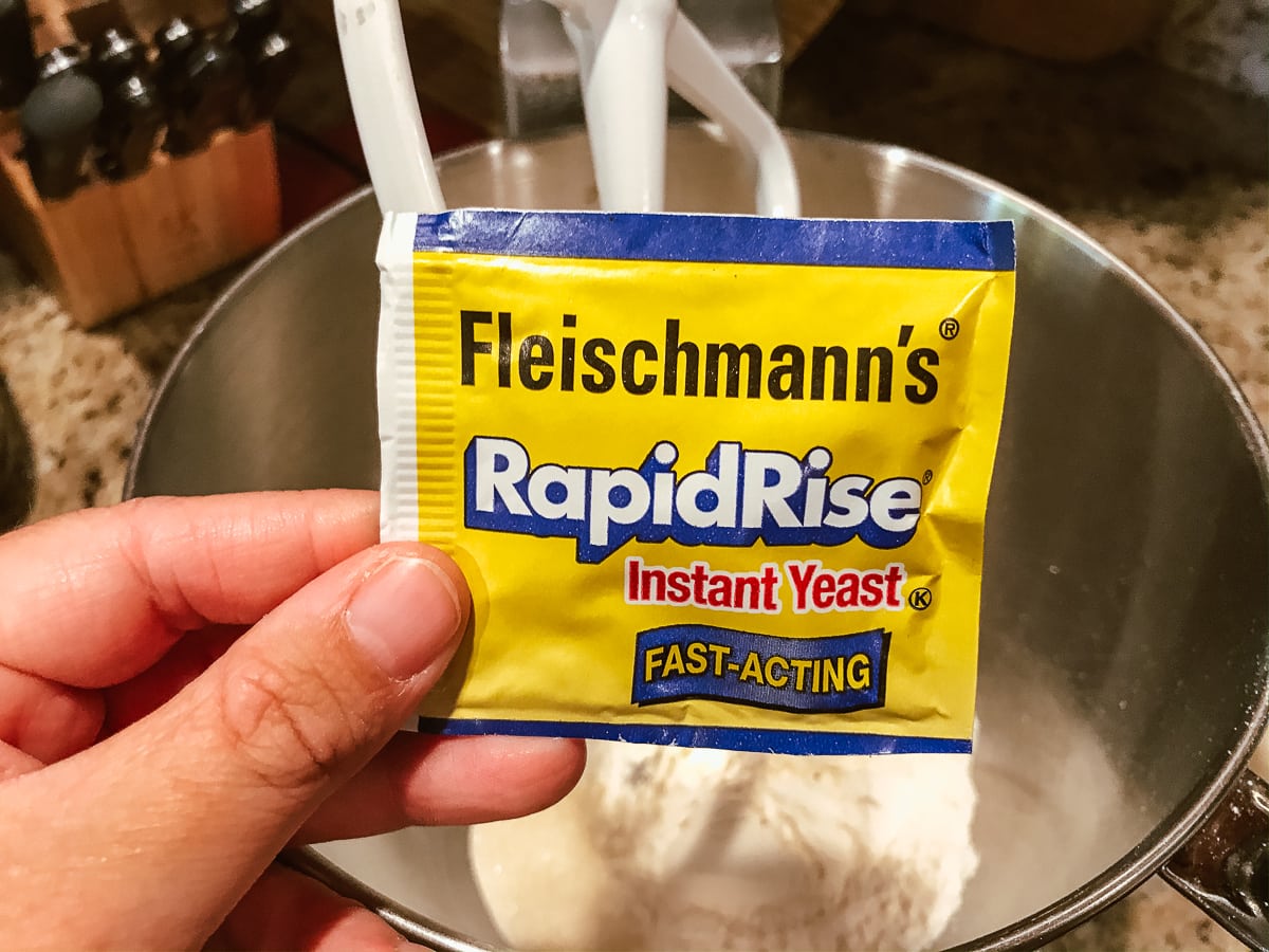 A hand holding a packat of RapidRise in front of a stand mixer.