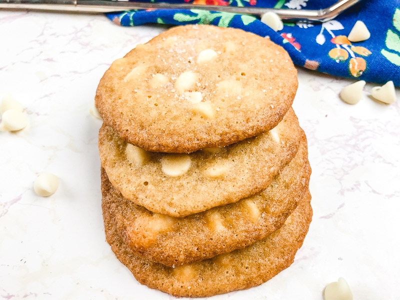 A stack of salted caramel white chocolate chip cookies with white chocolate chips scattered around.