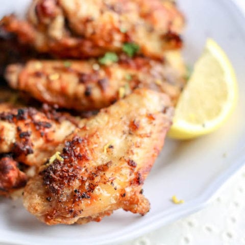 Air fryer wings on a white plate next to a lemon wedge.