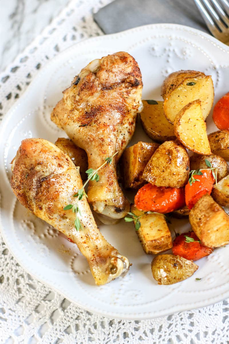 A white plate filled with drumsticks, potatoes, and carrots. 