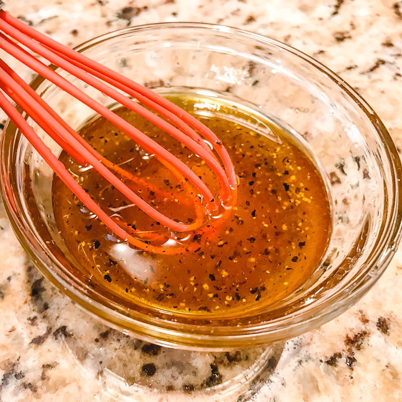 A whisk mixing up oil and maple syrup in a small glass bowl.