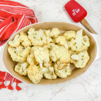 An oval serving dish filled with roasted cauliflower next to a silicone spoon that says "stir it up".