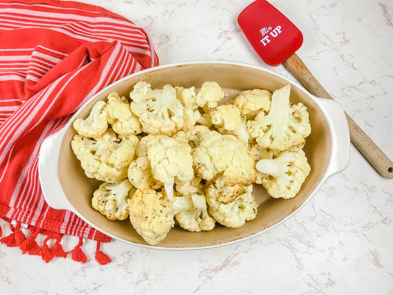 An oval serving dish filled with roasted cauliflower next to a silicone spoon that says "stir it up".