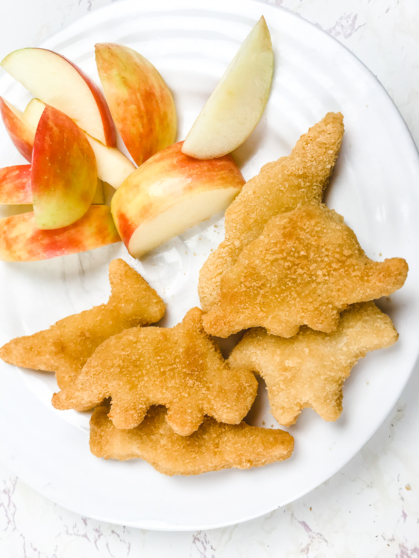 A white plate filled with air fried chicken nuggets and apple slices.