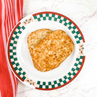 An apple printed plate with two air fried hashbrowns stacked on top of the plate.