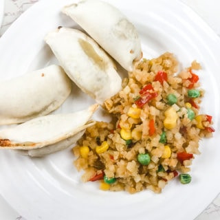 A white plate with air fried pot stickers and cauliflower fried rice.