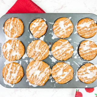 A muffin tin filled with cinnamon apple muffins next to an apple printed towel.