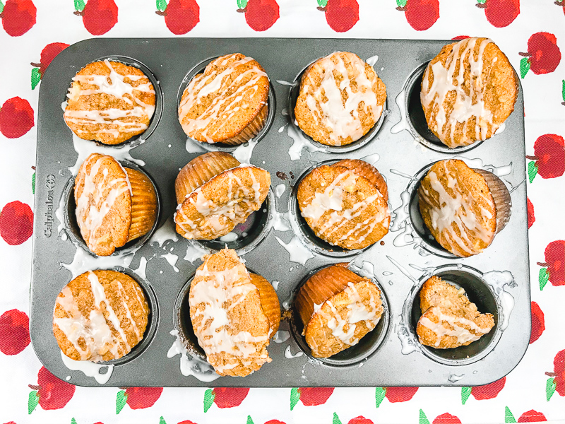 A muffin sheet filled with iced cinnamon apple muffins.