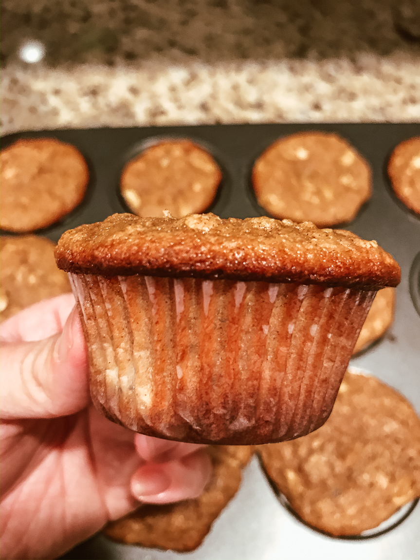 A hand holding a muffin sideways, showing the muffin top.