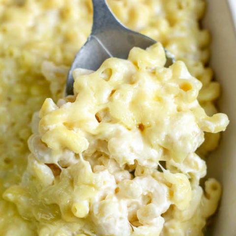 A serving spoon scooping up a heaping scoop of baked white cheddar mac and cheese.