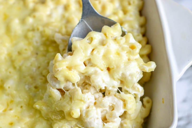 A serving spoon scooping up a heaping scoop of baked white cheddar mac and cheese.