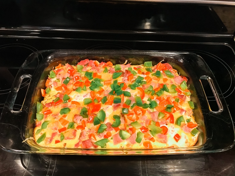 Baked casserole topped with shredded cheese and red and green diced bell peppers.