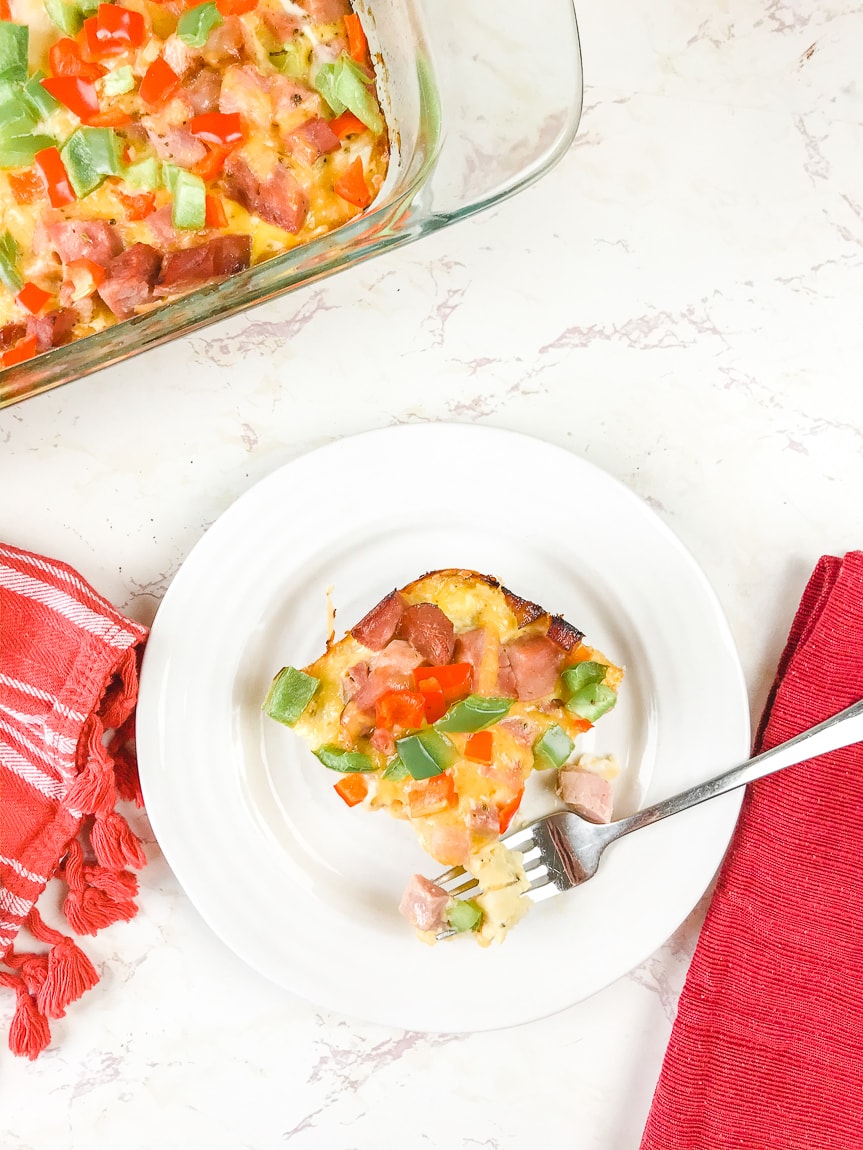 A fork laying on a plate with a bite of casserole on it.