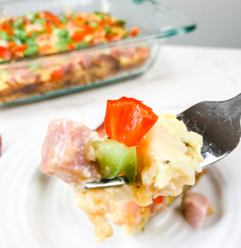 A forkful of breakfast casserole held up over the casserole dish.