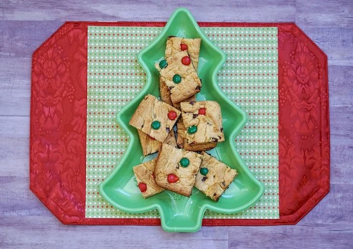 A red and green placemat with a green tree dish holding Christmas bar cookies.