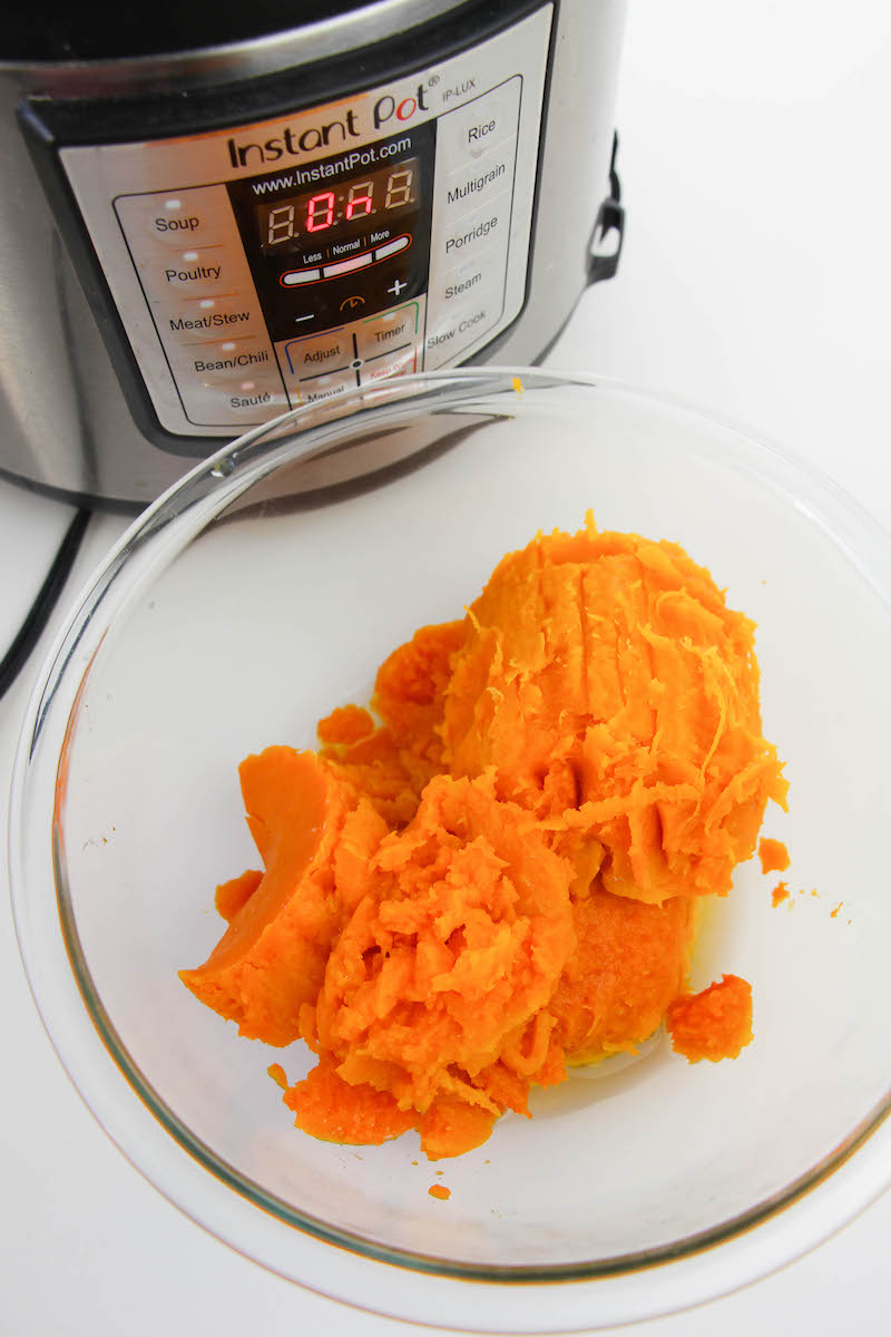 A glass bowl filled with cooked butternut squash in front of an instant pot.