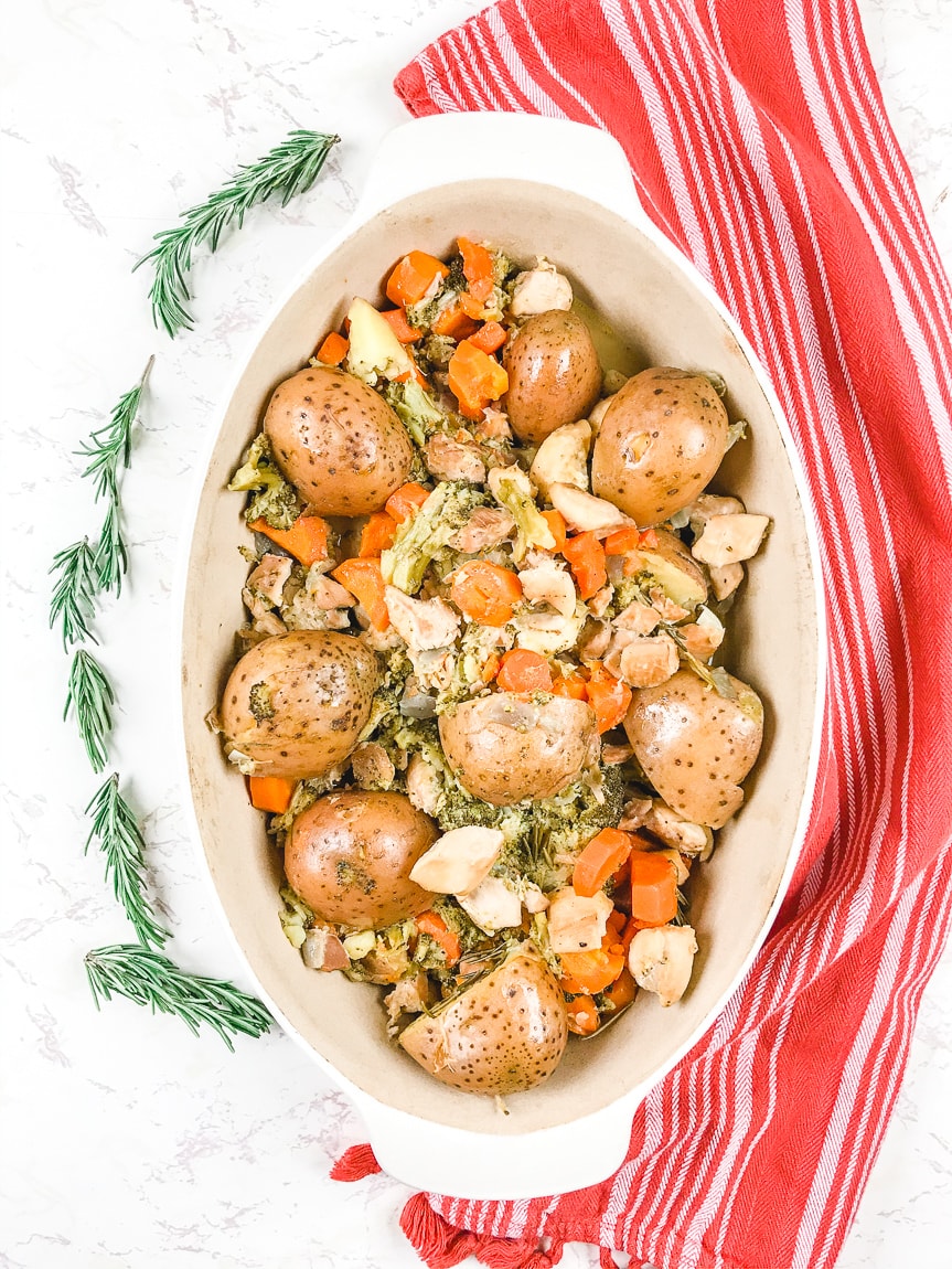 chicken and vegetables in oval serving dish with rosemary decoratively placed next to it.