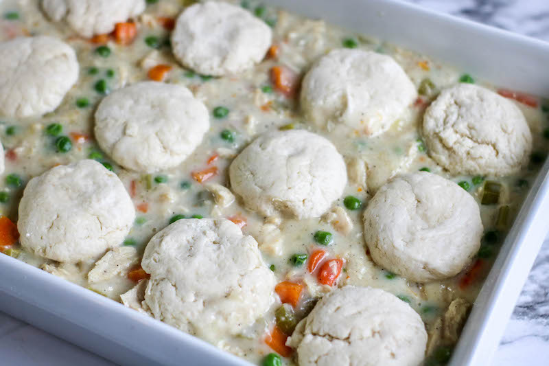 Biscuit dough on top of pot pie filling in baking dish.