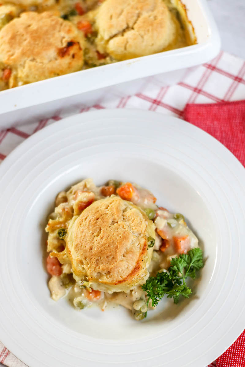 A serving of chicken pot pie on a white plate next to a baking dish of chicken pot pie.