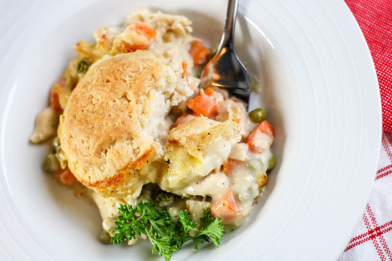Chicken pot pie topped with a biscuit and a fork stuck in for a bite.
