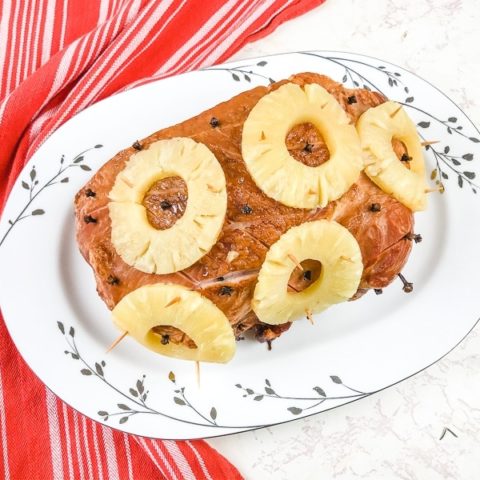 Ham covered in pineapple on white platter.