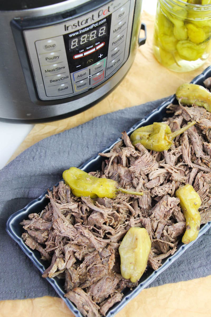 Overhead shot of Italian beef on a blue platter next to jar of peppers.