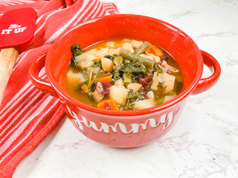 Red bowl that says "yummy" filled with minestrone soup.