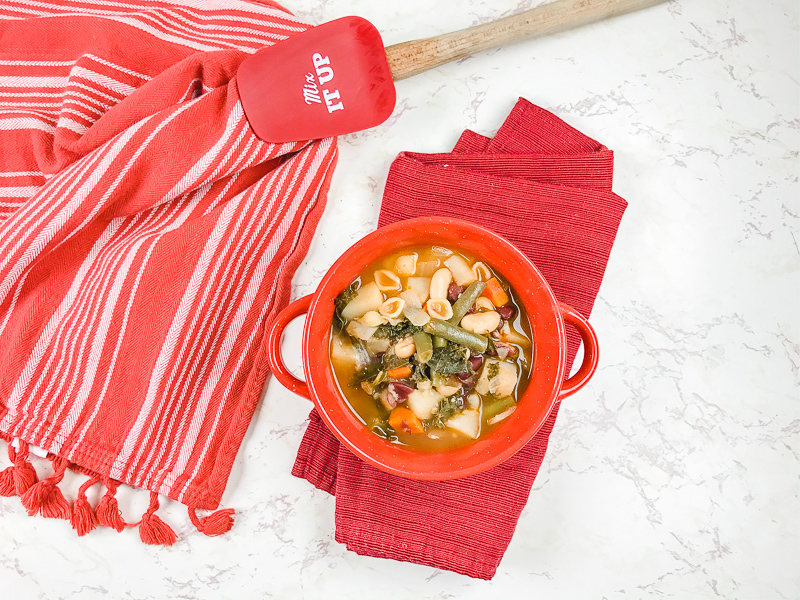 Overhead shot of bowl of soup on top of napkin and next to towel and silicone mixing spoon.