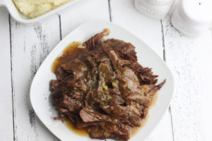 Overhead shot of roast beef with gravy on square plate.