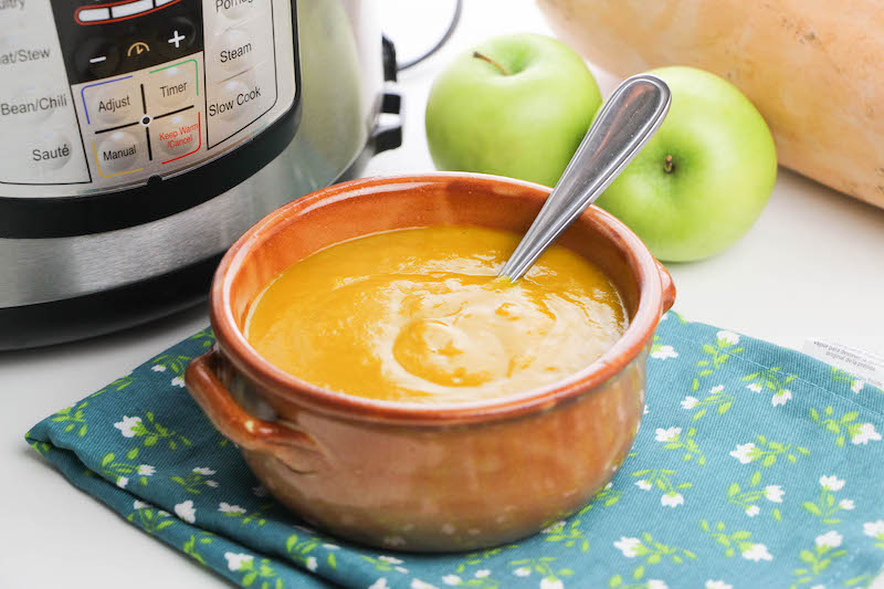 butternut squash soup in a red ceramic bowl in front of instant pot.