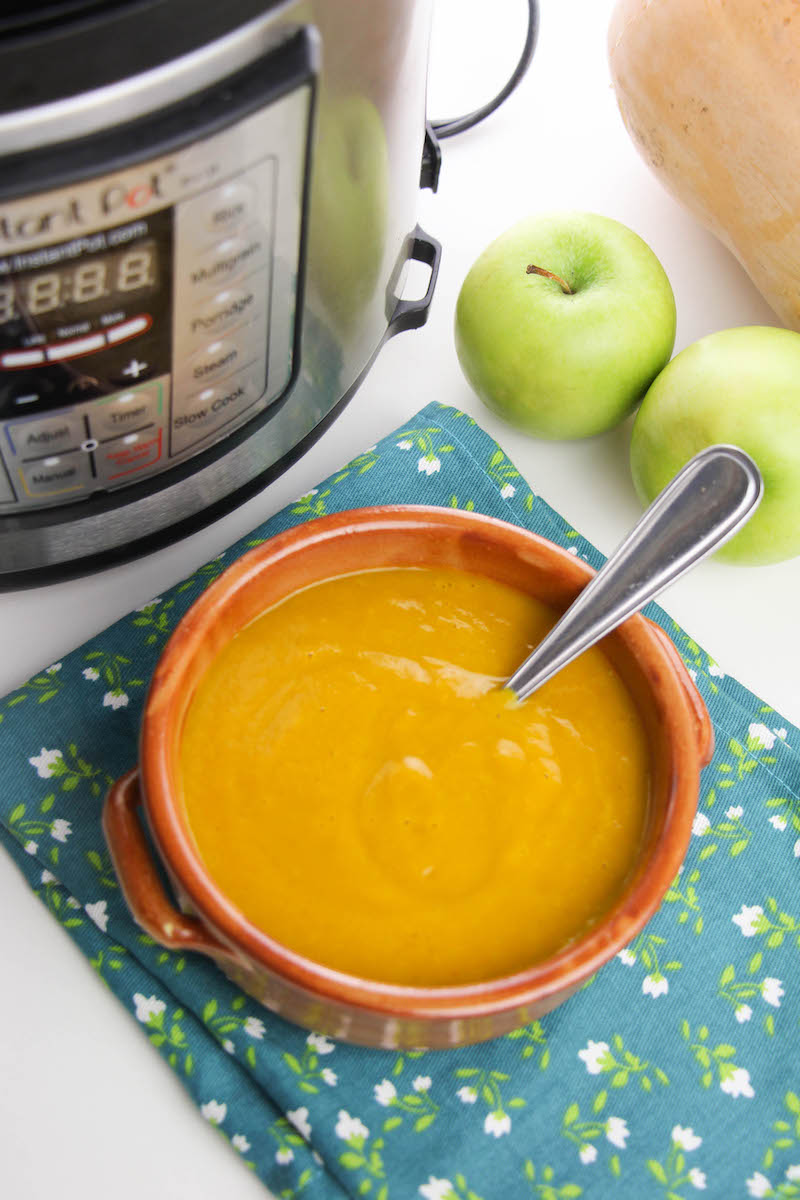 Overhead shot of butternut squash soup in bowl next to butternut squash, apples, and instant pot.