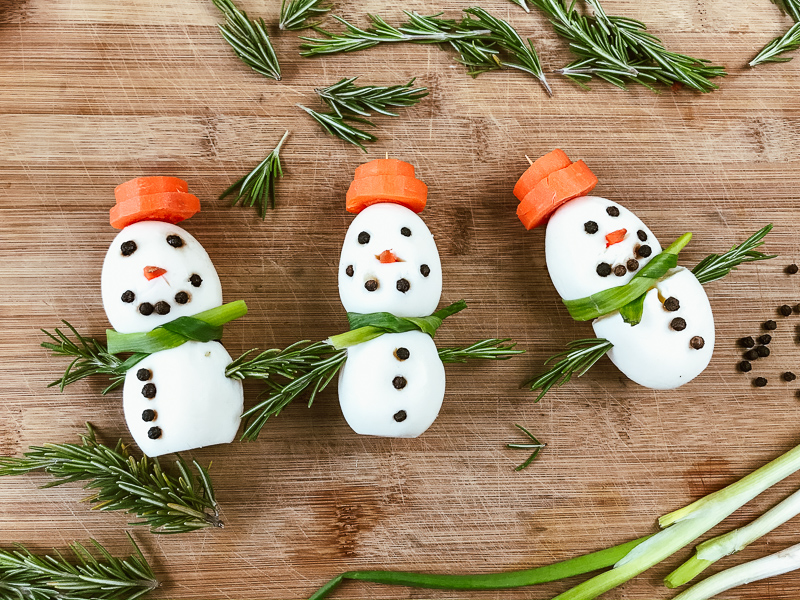 Three hard-boiled-egg snowmen on a wooden cutting board