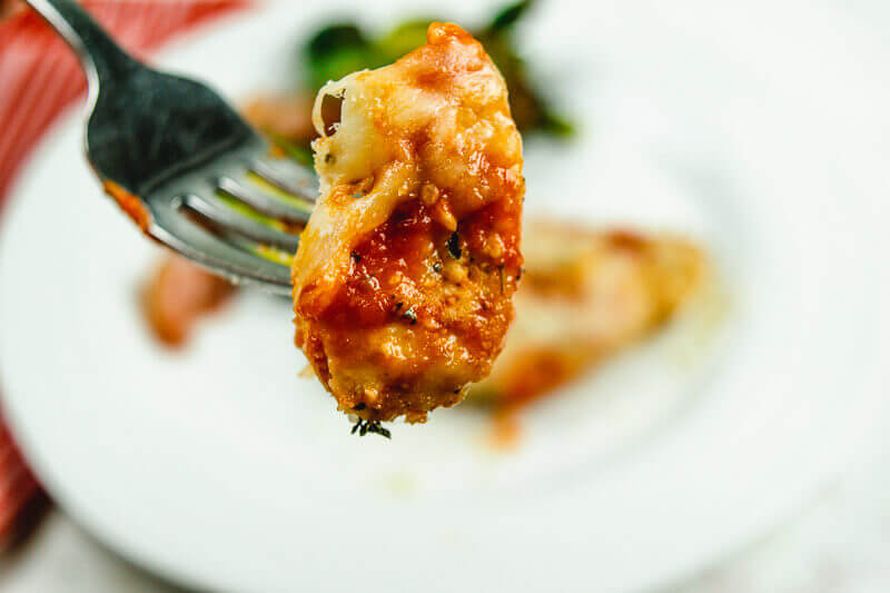 Close up of bite of chicken parmesan on a fork.