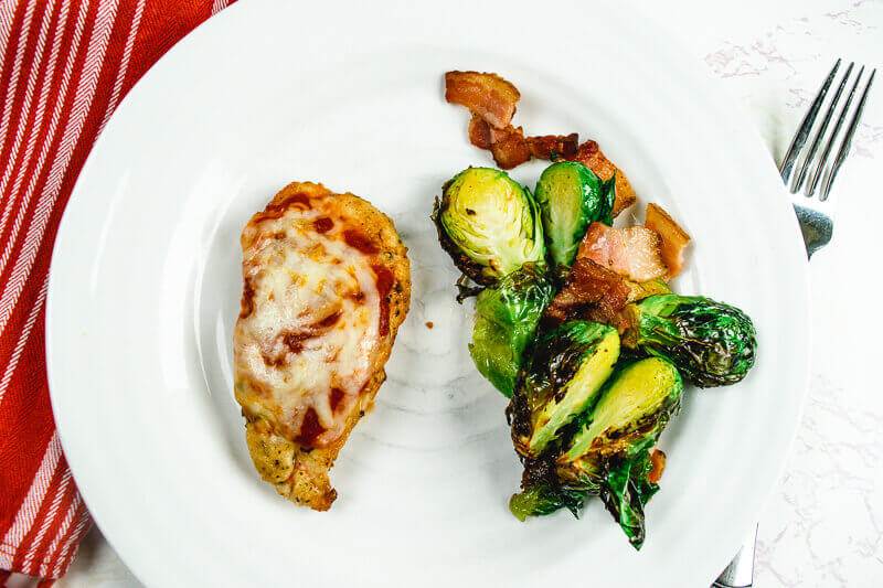 White plate of air fried chicken parmesan and brusssels sprouts.