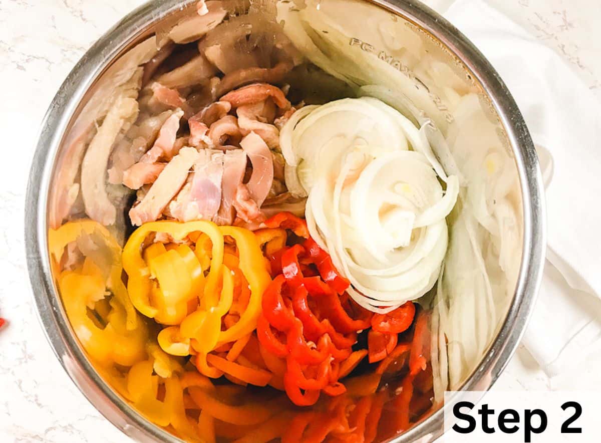 Sliced chicken, bell peppers, and onion inside a metal pot.