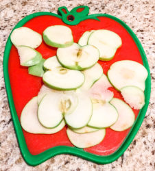 Apples sliced thinly on an apple shaped cutting board.