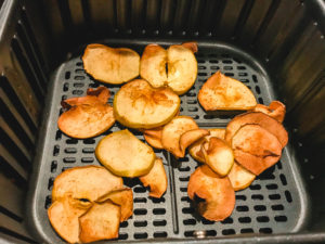 Cooked apple chips inside air fryer basket.