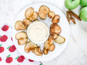 A white plate filled with apple chips arranged around a creamy beige dip.