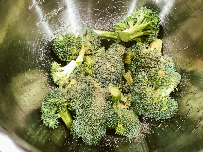Broccoli in a metal bowl topped with seasoning.