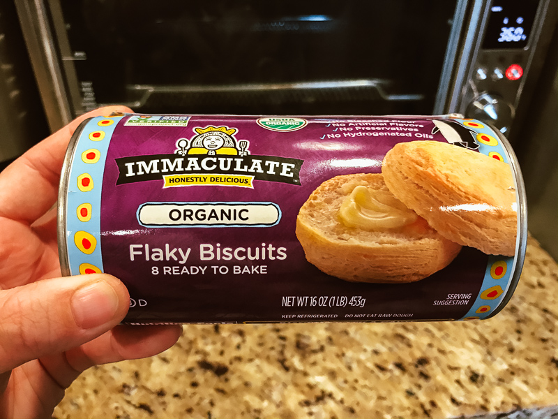 A can of biscuits held in front of an air fryer oven.