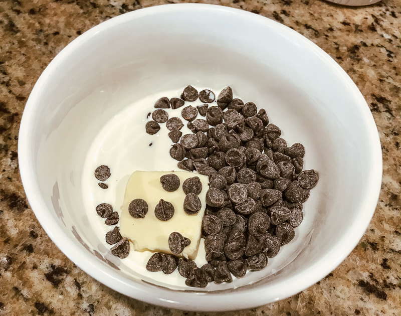 A white bowl with chocolate chips, cream, and butter. 