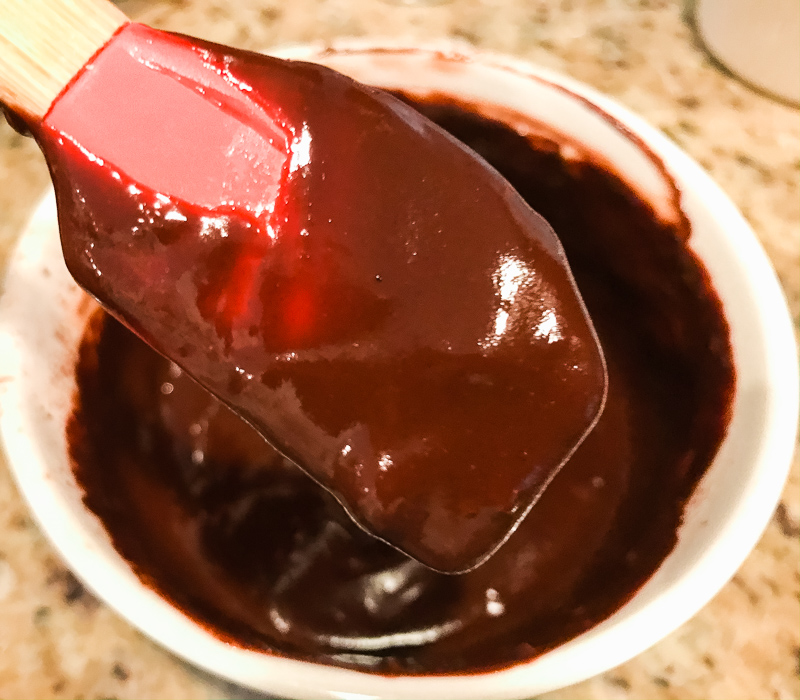 A spatula dipped in shiny chocolate frosting.