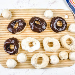 A cutting board filled with chocolate donuts, glazed donuts, and donut holes.